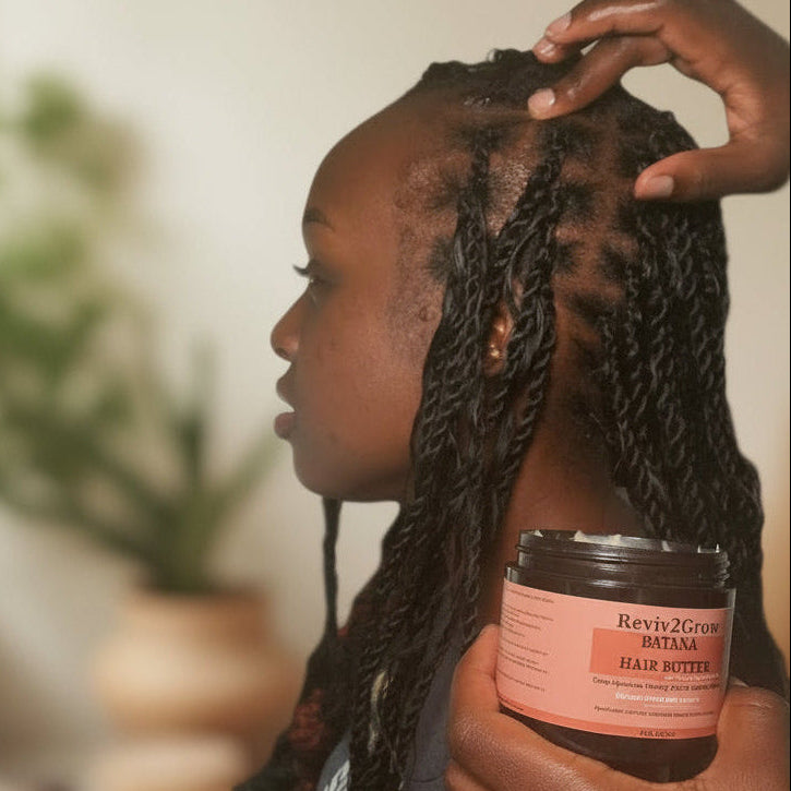 Person with braided hair holding a jar of Reviv2Grow Batana Hair Butter.