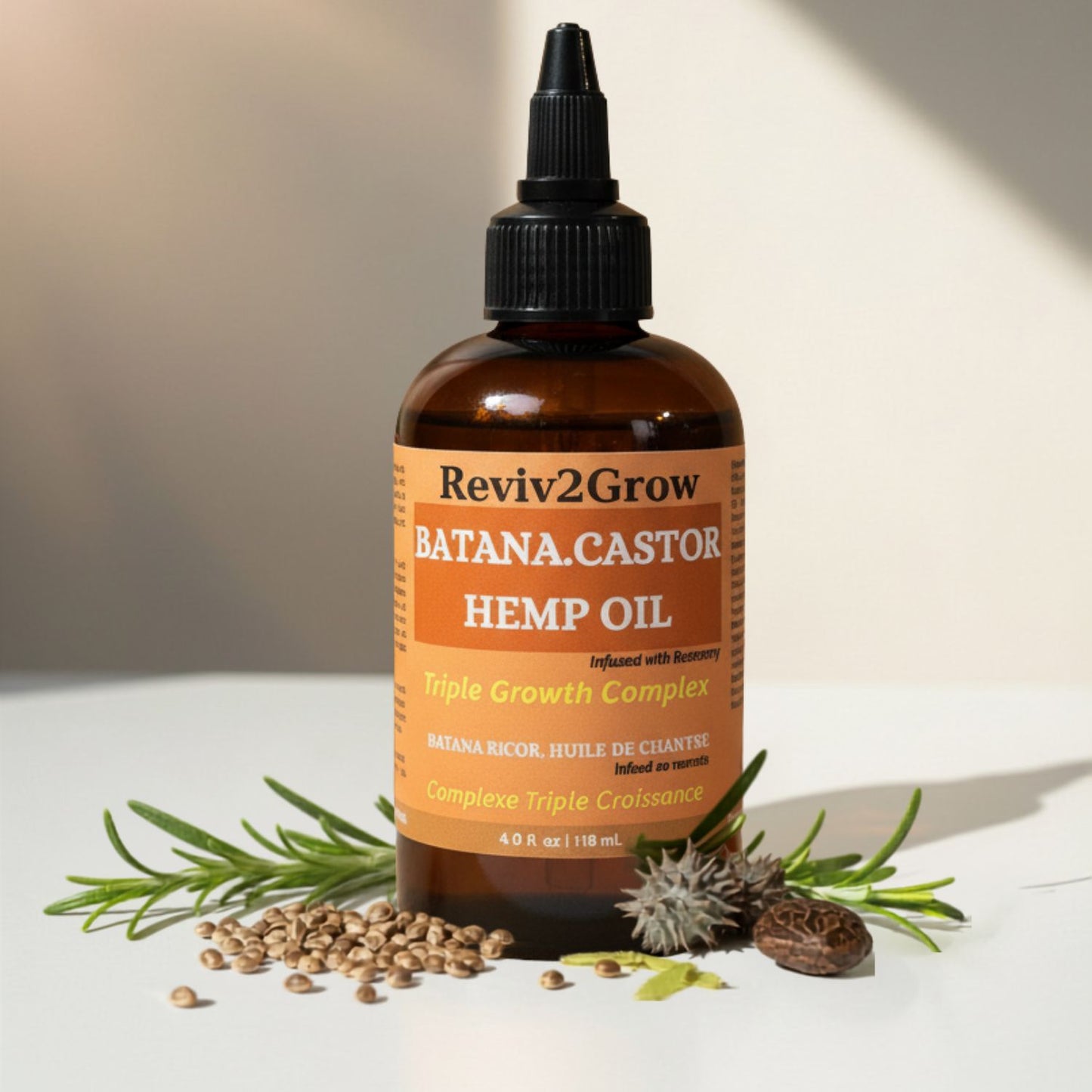 A bottle of Reviv2Grow Batana Castor Hemp Oil with botanical ingredients like rosemary, seeds, and a castor seed arranged around it on a white surface with a warm beige background.