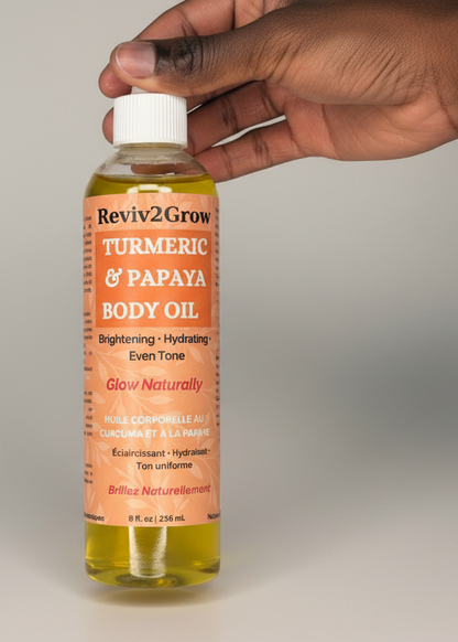 Hand holding a bottle of Reviv2Grow Turmeric & Papaya Body Oil against a neutral background